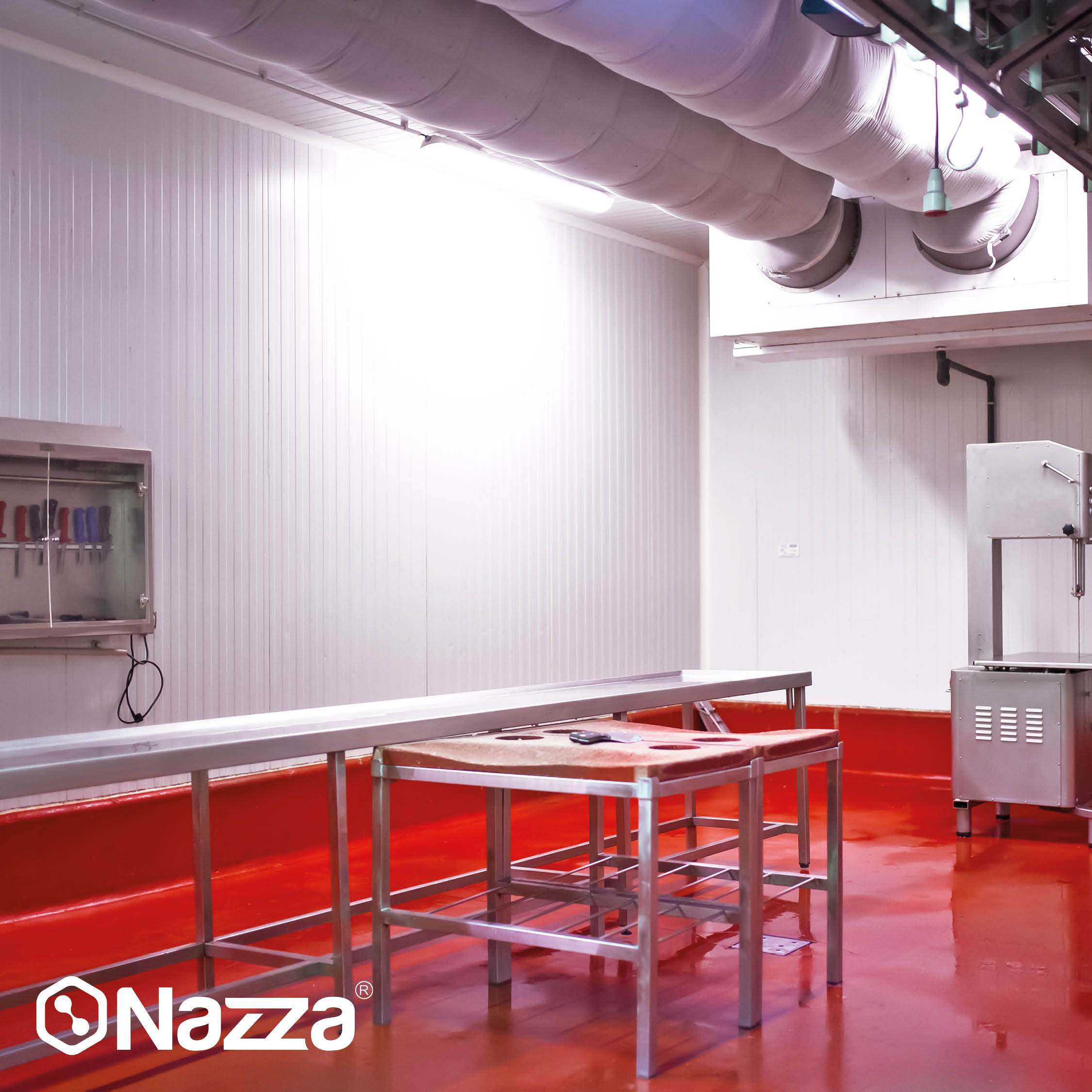 L’image montre une salle de découpe ou un espace de travail alimentaire avec des murs blancs et un sol rouge brillant, recouvert d’une peinture époxy alimentaire pour faciliter le nettoyage et l’hygiène. On voit des tables en acier inoxydable, une machine de découpe industrielle et, sur le mur, une armoire avec des couteaux organisés, ainsi que des conduits de ventilation au plafond.