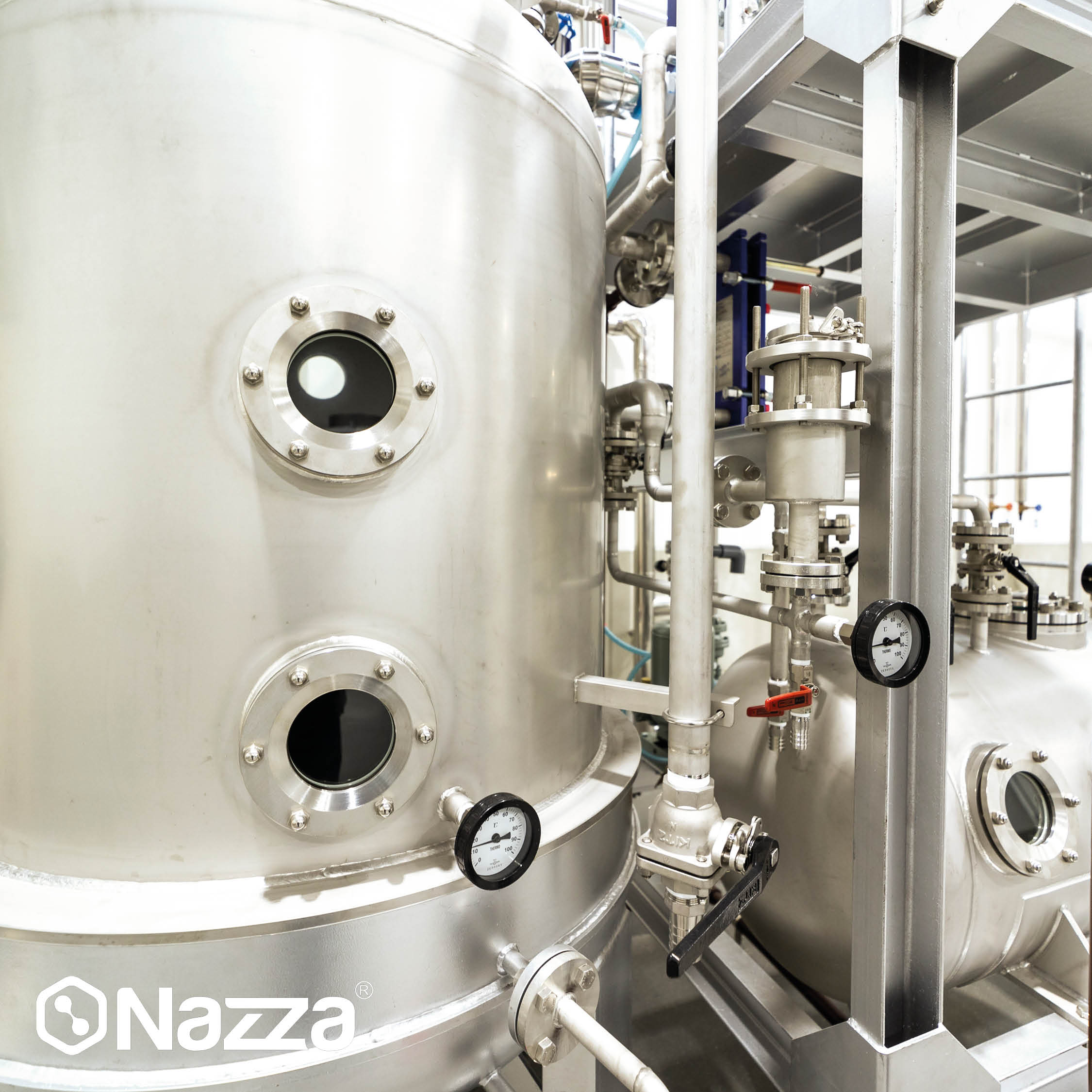 L’image montre un grand réservoir industriel en acier inoxydable avec plusieurs vannes, manomètres et connexions de tuyauterie. On distingue des hublots circulaires sur la surface de la cuve et une structure métallique qui soutient l’installation, typique des systèmes de stockage ou de traitement de liquides comme l’eau ou des produits alimentaires dans des environnements hygiéniques.